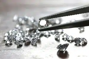 A photograph of a diamond being held with tweezers, with loose diamonds in the background