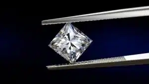 Princess cut diamond held with tweezers, sparkling.