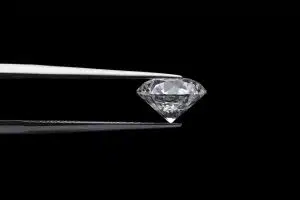 A photograph of a round brilliant cut diamond being held with tweezers against a black background